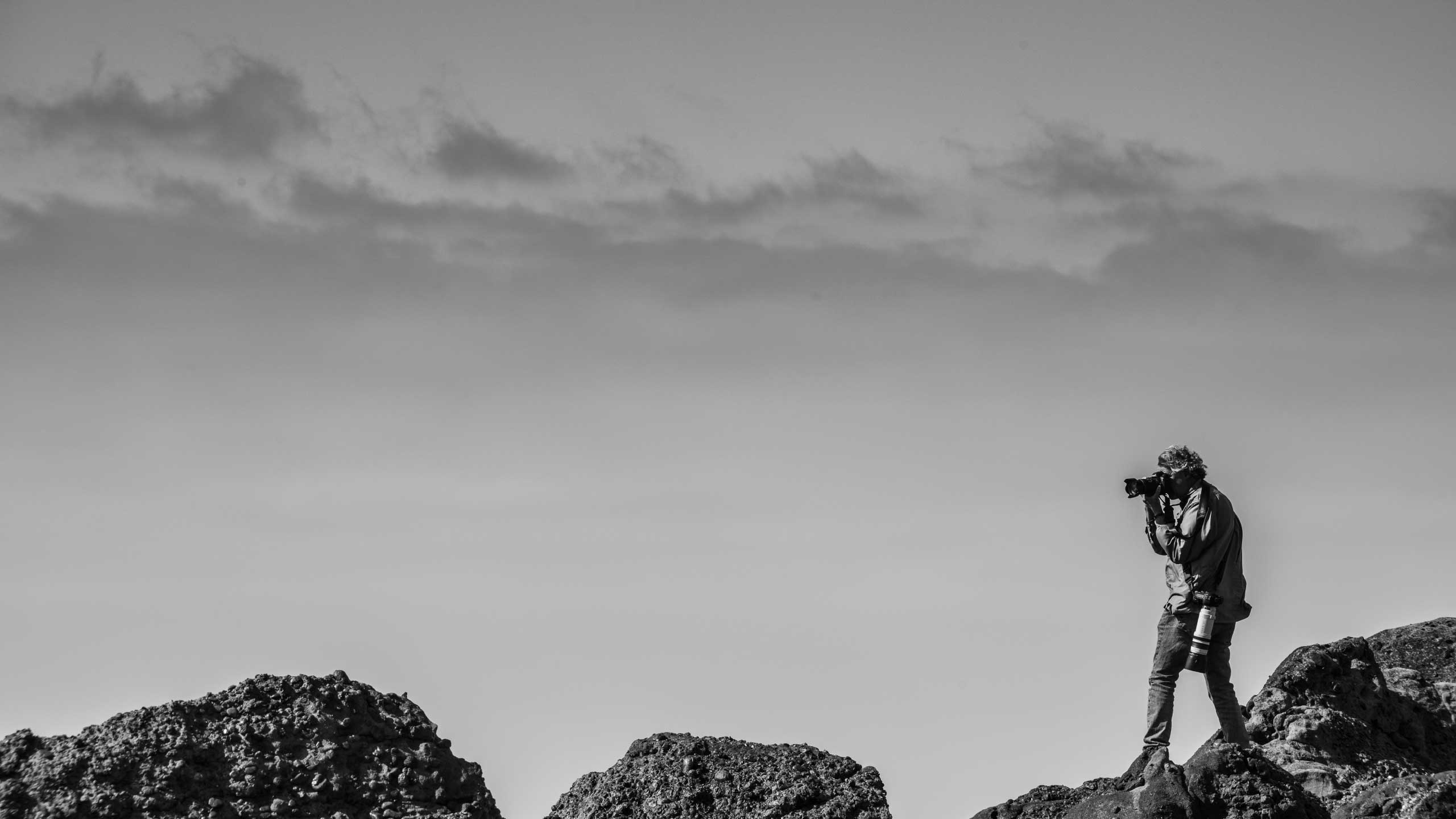 Black and white photo of Reinhard Ziegler shooting photos on a rock face